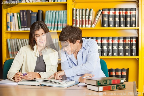 Image of Students Reading Book Together At Table In Library