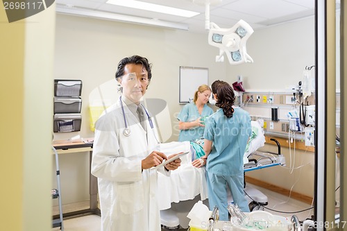 Image of Doctor Holding Digital Tablet With Nurses Examining Patient