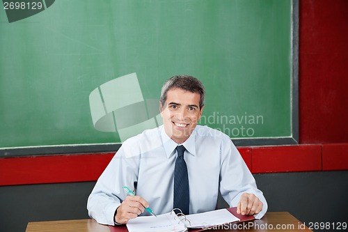 Image of Happy Teacher With Binder And Pen Sitting At Desk