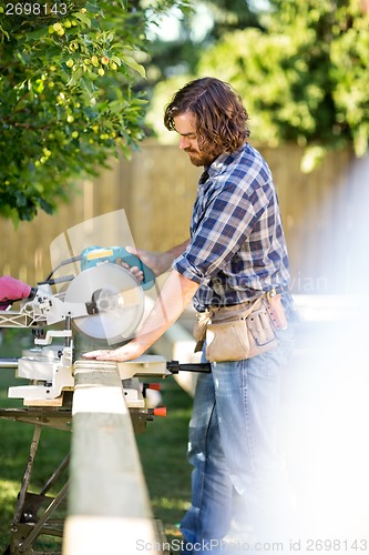 Image of Carpenter Using Table Saw To Cut Wooden Plank At Site