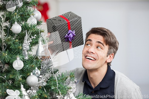 Image of Curious Man Holding Gift By Christmas Tree