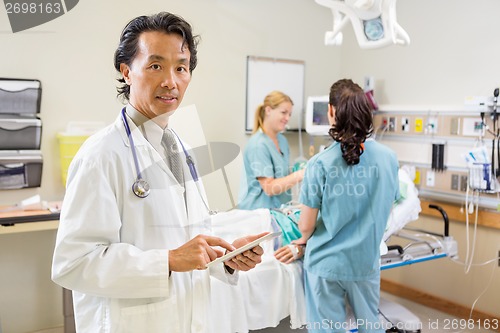 Image of Doctor Holding Digital Tablet While Nurses Examining Patient