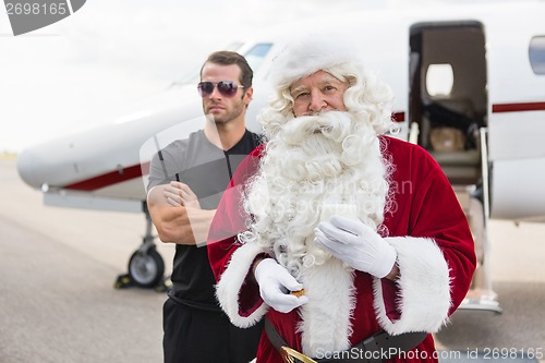 Image of Santa Holding Milk Glass By Bodyguard Against Private Jet