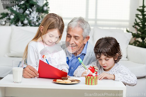 Image of Grandfather Assisting Children In Writing Letters To Santa Claus