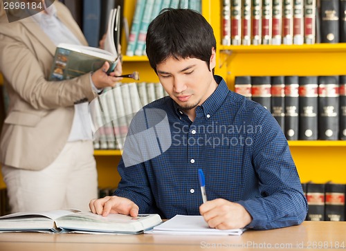 Image of Student Writing In Book At College Library