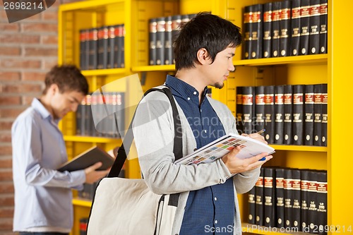 Image of Student Holding Books While Looking At Shelf In Library