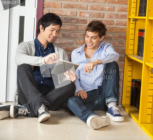 Image of Students Using Digital Tablet While Sitting By Bookshelf In Libr