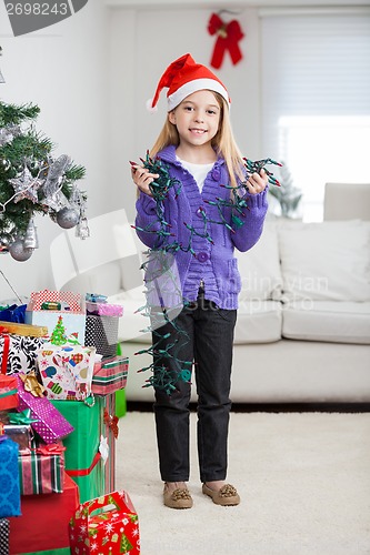 Image of Girl Holding Fairy Lights While Standing By Christmas Presents