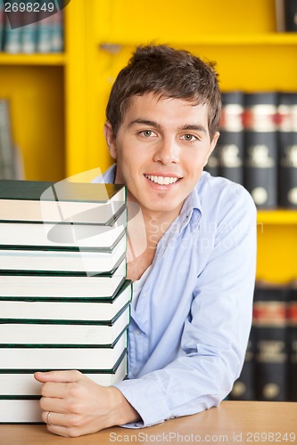 Image of Confident Man With Piled Books Smiling In College Library