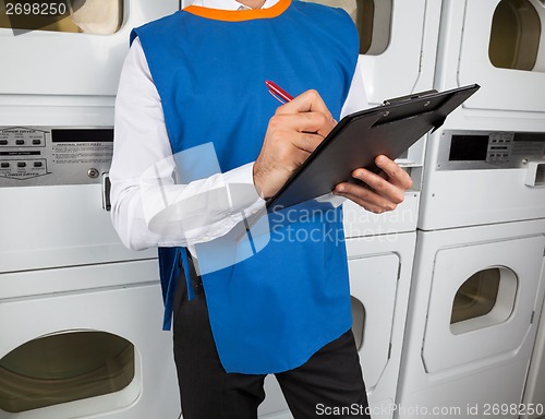 Image of Male Helper Writing On Clipboard In Laundromat