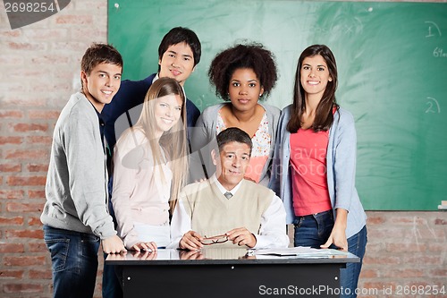 Image of Professor And Students At Desk Against Greenboard In Classroom