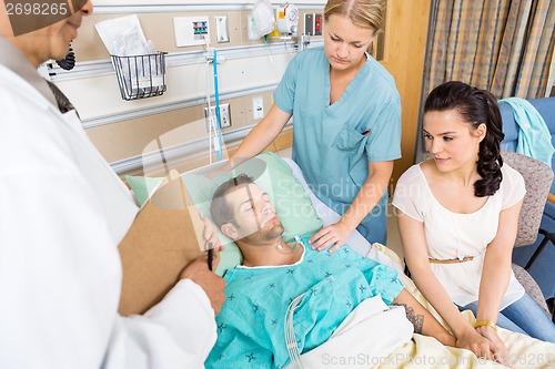 Image of Woman Holding Patient's Hand While Doctor And Nurse Examining Hi
