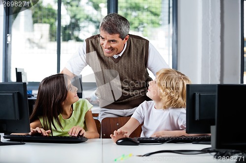 Image of Teacher Assisting Schoolchildren In Using Desktop Pc