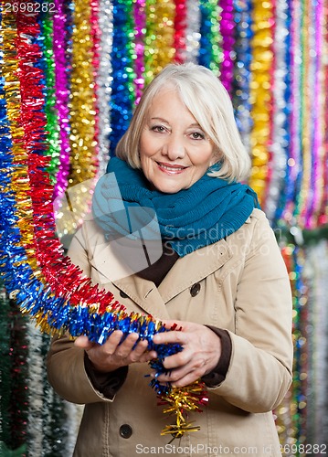 Image of Senior Woman Holding Tinsels At Christmas Store