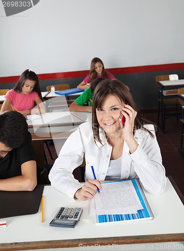 Image of Teenage Schoolgirl Using Cellphone While Writing At Desk