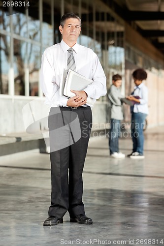 Image of Mature Professor With Books Standing On College Campus