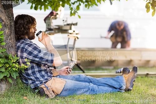 Image of Carpenter Using Mobilephone While Drinking Coffee From Disposabl