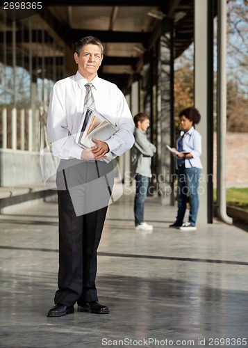 Image of Mature Teacher With Books Standing On University Campus