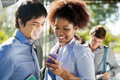 Image of Friends Reading Text Message On Cellphone In Campus