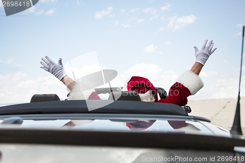 Image of Santa With Arms Raised In Convertible Against Sky
