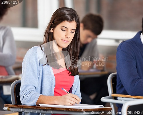 Image of Woman Writing On Book At Desk In Classroom