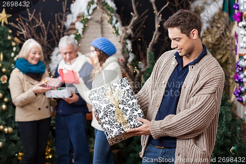 Image of Man Looking At Christmas Present With Family In Background