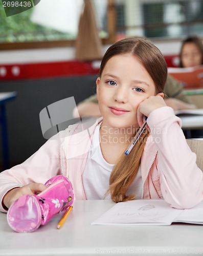 Image of Schoolgirl Sitting With Pouch At Desk In Classroom
