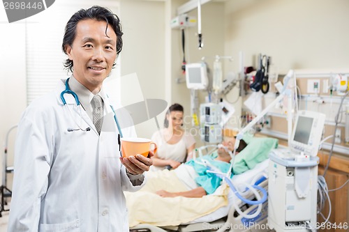Image of Doctor Holding Coffee Cup With Patient Resting On Bed