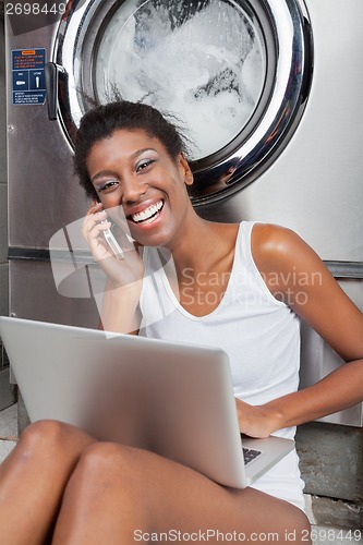 Image of Woman With Laptop Using Mobilephone In Laundry