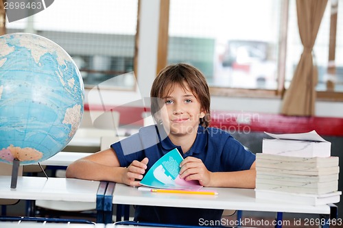 Image of Schoolboy Sitting With Books And Globe At Desk