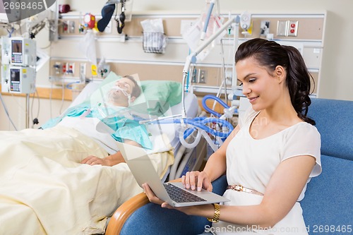 Image of Woman Using Laptop While Sitting By Patient Resting In Bed