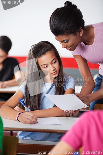 Image of Teacher Showing Paper To Female University Student At Desk