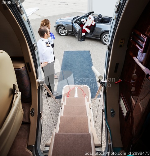 Image of Santa Waving In Convertible With Pilot And Airhostess In Foregro