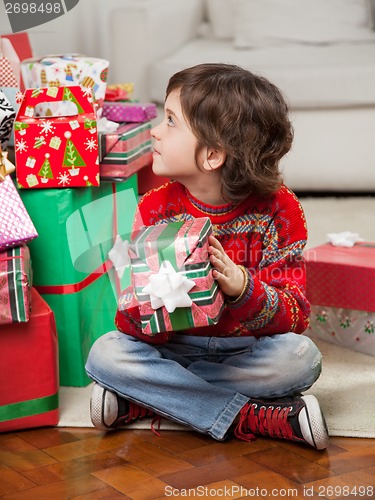 Image of Boy Holding Christmas Gift While Sitting On Floor