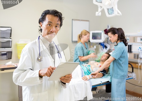 Image of Doctor Using Digital Tablet While Nurses Treating Patient