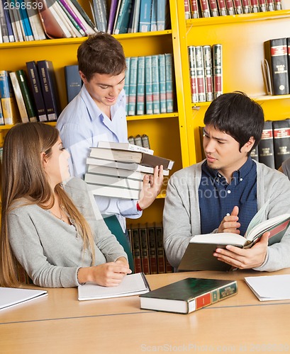 Image of Student Carrying Books While Friends Sitting In Library
