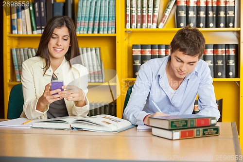 Image of Student Studying While Friend Using Mobilephone In Library