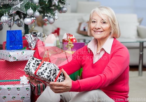Image of Senior Woman Sitting By Stack Of Christmas Presents