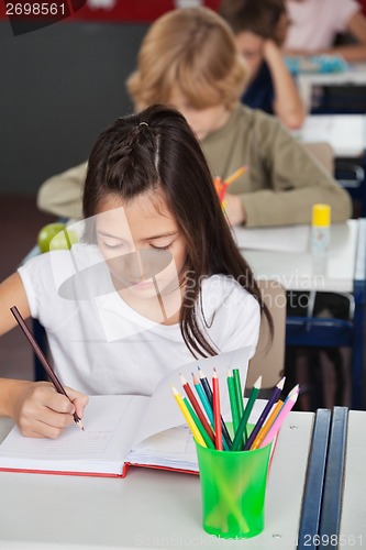 Image of Schoolgirl Writing In Book At Classroom