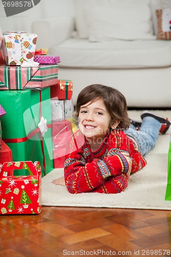 Image of Happy Boy Lying Besides Stacked Christmas Gifts