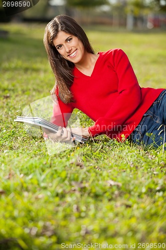 Image of Woman Holding Books While Relaxing On Grass At Campus