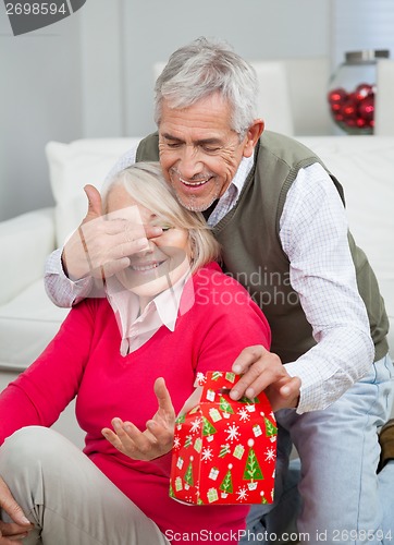 Image of Senior Man Covering Woman's Eyes While Giving Christmas Gift