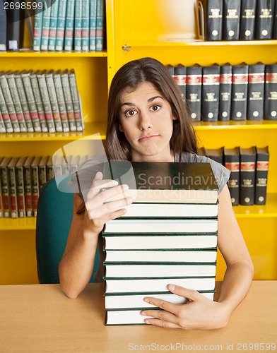 Image of Confused Student With Stacked Books Sitting At Table In Library