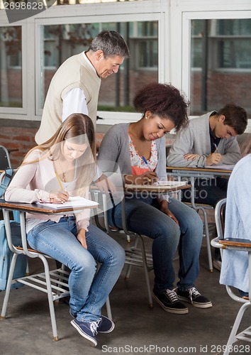 Image of Students Writing Exam While Professor Supervising Them In Classr