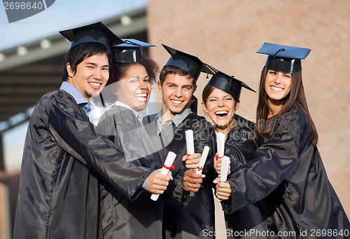 Image of Students In Graduation Gowns Showing Diplomas On Campus