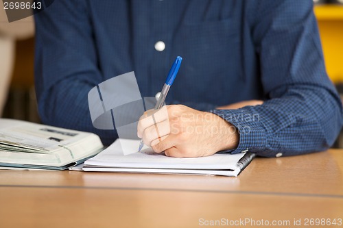 Image of Male Student Writing In Book At Library