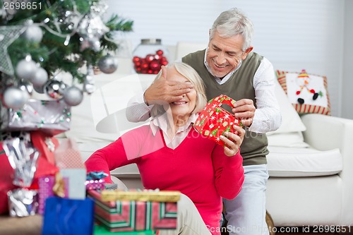 Image of Happy Man Covering Woman's Eyes While Giving Christmas Gift