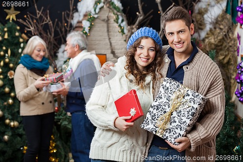 Image of Happy Couple Holding Christmas Presents With Parents In Backgrou