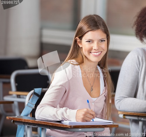Image of University Student Sitting At Desk With Friend In Classroom