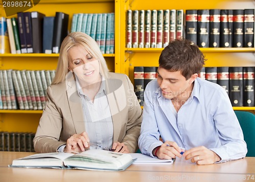 Image of Teacher Explaining Student While Sitting At Table In Library